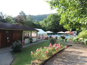 Wohnwagen und Gartenweg auf dem Campingplatz, mit Blumenbeet, Sitzgelegenheiten und Bäumen im Hintergrund.