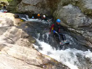 Rafting-Gruppe auf dem Fluss mit Schlauchboot, Helmen und Paddeln zwischen Felsen und Stromschnellen.