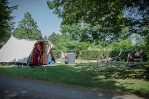 Zelt auf einem Campingplatz im Grünen, daneben Gartenmöbel und ein weiterer Stellplatz mit Wäscheleine und Bäumen.