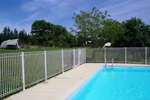 Campingpool auf der Terrasse, Zelt im Garten und Heckenzaun vor grünen Bäumen unter blauem Himmel.