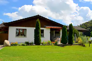 Ferienhaus mit Terrasse, Rasenfläche und hohen Zypressen im Garten, mit Sitzbereich und Fenstern am Gebäude.