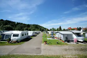 Reihe von Wohnwagen und Zelten auf einem Campingplatz, mit Rasen, Gartenmöbeln und einem Weg zwischen den Stellplätzen.