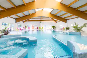 Überdachter Campingpool mit Holzdecke, Treppenstufen und Liegen am Beckenrand, im Hintergrund Pflanzen und Sitzbereiche.