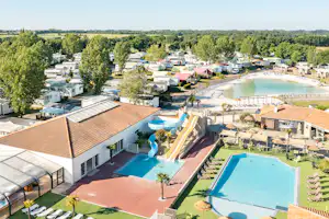 Blick auf einen Campingplatz mit zwei Pools, Liegen und Wegen zwischen Wohnmobilen und Bungalows, umgeben von Bäumen und See.