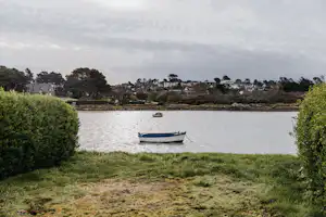 Blick auf das Seeufer mit Motorboot im Wasser, Rasen und Büschen im Vordergrund sowie Häusern und Bäumen am Ufer.