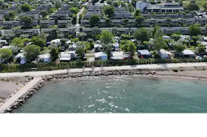 Luftaufnahme eines Campingplatzes am See mit vielen Stellplätzen, Wohnwagen und Bungalows entlang der Uferpromenade.