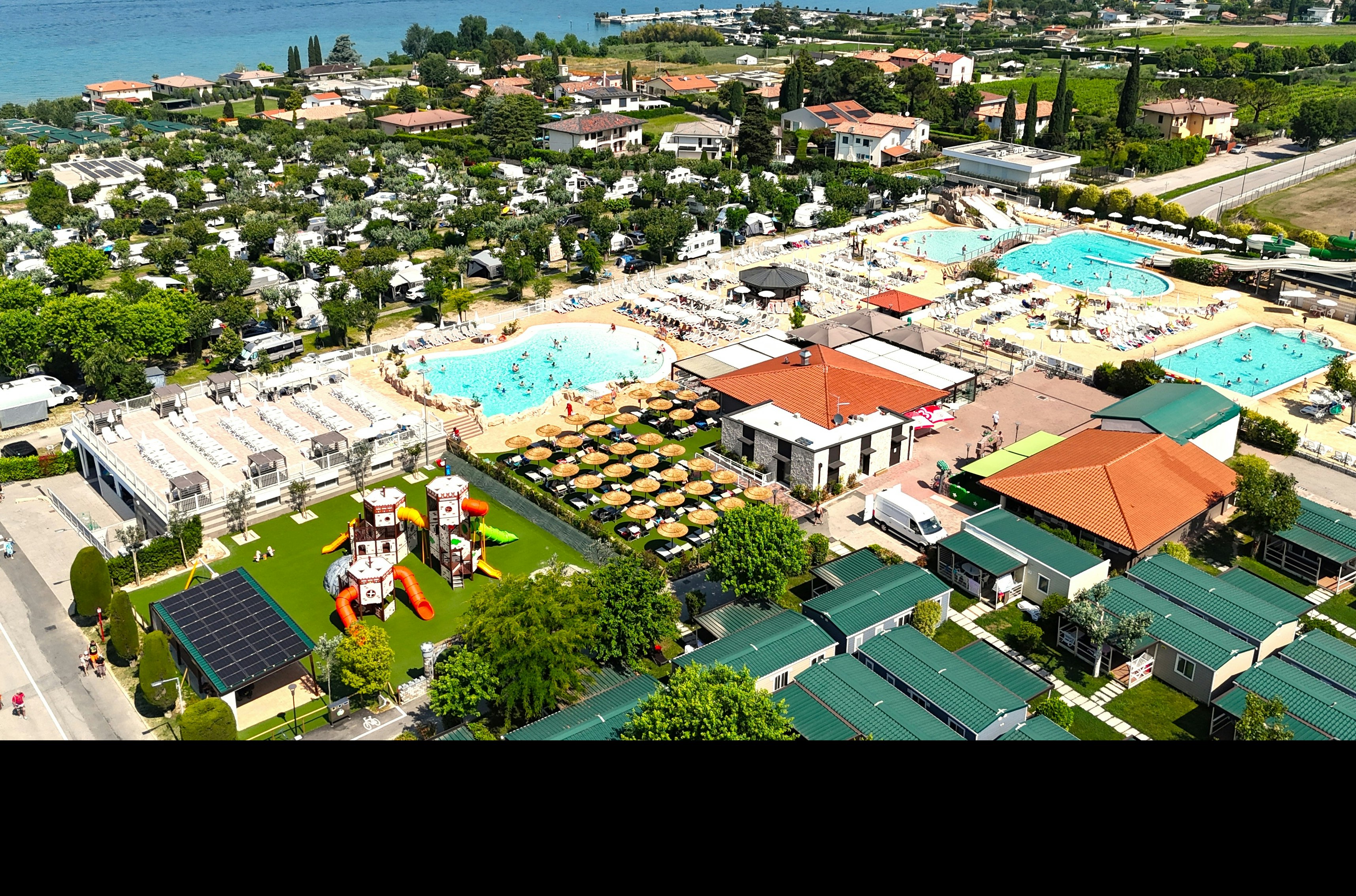 Campinganlage mit mehreren Wohnmobilen und Zelten, grünen Parzellen, zwei türkisfarbenen Pools und orangefarbenen Gebäuden am Hang.