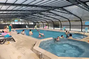 Überdachtes Schwimmbecken auf dem Campingplatz, Menschen im Wasser, Liegen und Stühle am Beckenrand.