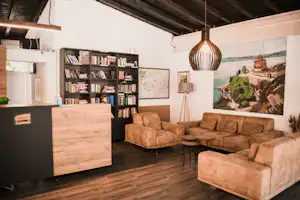 Wohnbereich im Campinghaus mit beigem Sofa, Bücherregal, Stehtisch und Hängelampe über dem Sitzbereich.
