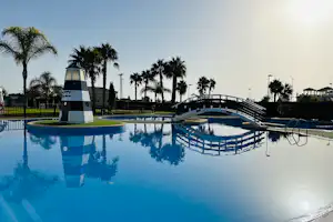 Großer Camping-Pool mit Liegen und Sonnenschirmen, Palmen im Hintergrund und Blick auf das Poolgeländer.