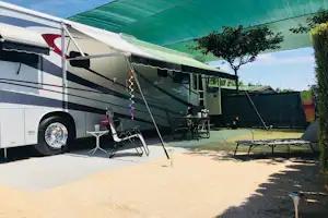 Wohnmobil mit Vorzelt und Markise, Campingstühle und Tisch auf dem Stellplatz, daneben ein grünes Zelt und Bäume.