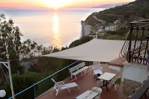 Terrasse am Campingplatz mit Sonnenschirm, Liegen und Tisch, Blick auf das Meer und die Küste bei Sonnenuntergang.