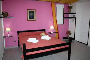 Bett mit roten Decken und weißen Handtüchern in einem Campingzimmer mit lila Wand, Nachttischen und Lampen.