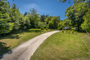 Schotterweg durch eine grüne Campinganlage, umgeben von Bäumen und Rasenflächen unter blauem Himmel.