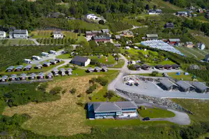 Luftaufnahme einer Campinganlage mit roten Ferienhäusern, Stellplätzen, Wohnmobilen und Zelten in grüner Hügellandschaft.