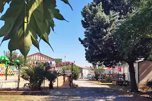Weg auf einem Campingplatz zwischen Bäumen, mit Wohnwagen und kleinen Gebäuden am Rand.