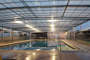 Überdachtes Schwimmbecken im Innenbereich mit Glasdach, Sonnenliegen und Umrandung aus Fliesen.