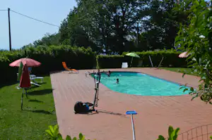 Camping-Pool im Garten mit Sonnenschirmen, Liegestühlen und gepflasterter Terrasse, umgeben von Hecken und Bäumen.
