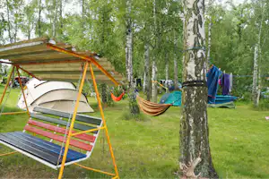 Campingplatz mit Hängematte und mehreren Zelten im Grünen, neben einem Holzrahmen mit Liegefläche zwischen Birken.
