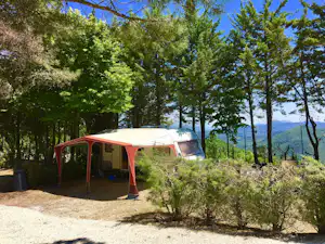 Wohnmobil mit Vorzelt auf einem Campingplatz im Grünen, umgeben von Bäumen und mit Blick auf Berge in der Ferne.