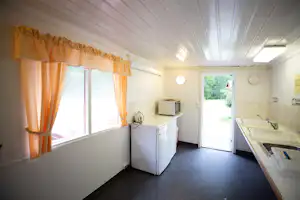 Innenansicht eines Wohnwagens mit Küchenzeile, Kühlschrank, Herd und Esstisch, daneben große Tür zum Außenbereich.