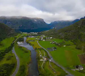Campingplatz im Tal mit Fluss, Wiesen und Zufahrtsstraßen, umgeben von Bergen und bewaldeten Hängen.