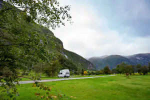 Wohnmobil auf einer grünen Wiese am Campingplatz, umgeben von Bäumen und Bergen im Tal.