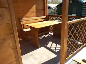 Holzterrasse am Campingplatz mit Tisch und Bänken, umgeben von Holzwänden und einem Geländer.