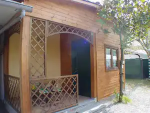 Holzbungalow mit Veranda, Holzgeländer und Eingangstür, daneben Fenster und Gartenweg am Campingplatz.