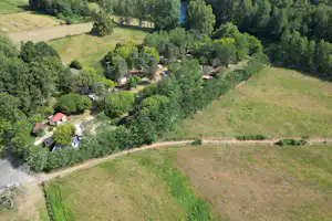 Luftaufnahme eines Campingplatzes im Grünen mit Wegen, Bäumen, mehreren Stellplätzen und Wohnwagen sowie einem kleinen Gebäude.