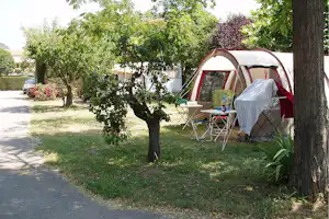 Campingzelt mit Vorzelt und Tisch am Stellplatz, umgeben von Bäumen und Rasen neben dem Weg.