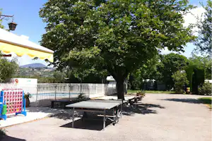 Terrasse mit Tisch und Bank unter einem großen Baum, daneben ein weißer Zaun und ein Wohnwagenstellplatz.