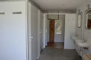 Modernes Badezimmer mit Waschbecken, Fliesenboden und geöffnetem Zugang zur Dusche, weiße Wände und Spiegelschrank.