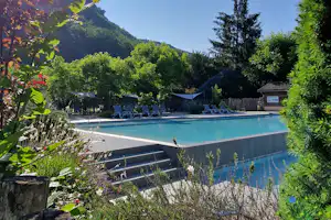 Schwimmbecken im Campingbereich mit Liegestühlen, umgeben von Grün und Bergen im Hintergrund.