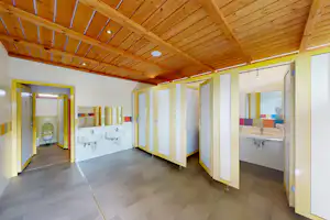 Heller Flur in einem Camping-Unterkunftsgebäude mit Holzdecke, grauem Boden und mehreren Türen sowie Küchenzeile.
