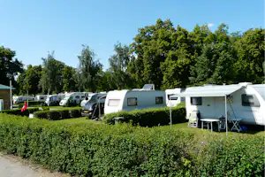 Reihe von Wohnwagen und Caravans auf einem Campingplatz, mit Hecken, Rasen und Sitzgarnitur vor einem Wohnwagen.