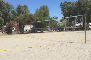 Volleyballfeld auf einem Campingplatz mit Netz, Sandboden und Bäumen im Hintergrund.