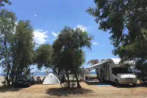 Zelt und Wohnmobil auf dem Campingplatz zwischen Bäumen, mit Auto und Tisch im Hintergrund.