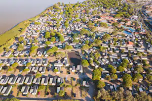 Luftaufnahme eines Campingplatzes mit vielen Stellplätzen, Wohnwagen und Mobilheimen am See, umgeben von Bäumen und Wegen.