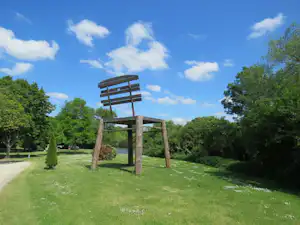 Holzschaukel auf einer grünen Wiese im Campingbereich, umgeben von Bäumen und einem Weg.