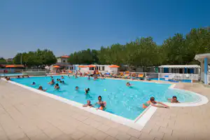 Schwimmbad mit mehreren Liegen und Sonnenschirmen, Menschen im Wasser und Beckenrand aus hellem Pflaster.