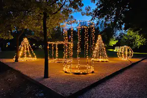 Campingplatz im Abendlicht mit beleuchteten Weihnachtsfiguren im Garten, Bäume und Wege zwischen den Lichtinstallationen.