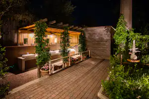 Außenbereich mit mehreren Waschbecken auf einer Terrasse, Holzverkleidung und Sichtschutzzaun, umgeben von Bäumen und Pflanzen.