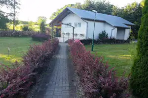 Campinghaus mit Terrasse, gepflastertem Weg und Ziersträuchern im Garten, umgeben von Bäumen und Hecken.
