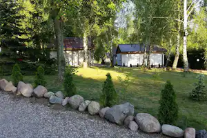 Weiße Ferienhäuser im Grünen mit gepflegtem Rasen, Kiesweg und Steinkante am Rand, umgeben von hohen Bäumen.