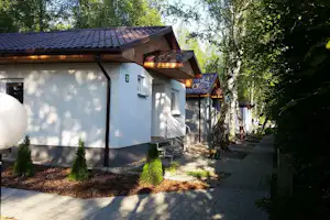 Campinghaus mit Holzveranda und Sitzbank, gepflasterter Weg und kleine Sträucher vor dem Gebäude im Grünen.