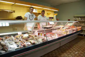 Theke im Camping-Bistro mit zwei Mitarbeitern, hinter Glas Salami, Käse und Gläsern mit Aufstrichen.