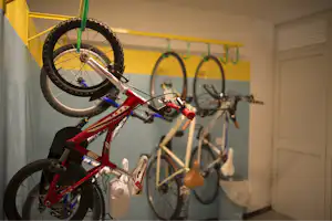 Rote Kinderfahrräder und weitere Fahrräder in einem Abstellraum, mit gelben Wänden und grünen Haken an der Wand.