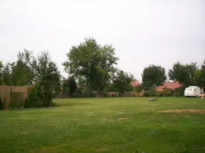 Grünes Campinggrundstück mit Rasenfläche, Hecken und Bäumen; ein Wohnwagen steht am Rand des Platzes.