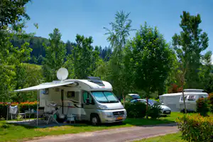 Wohnmobil auf dem Stellplatz mit Vorzelt, Campingstühlen und Tisch, umgeben von Bäumen und Wiese.